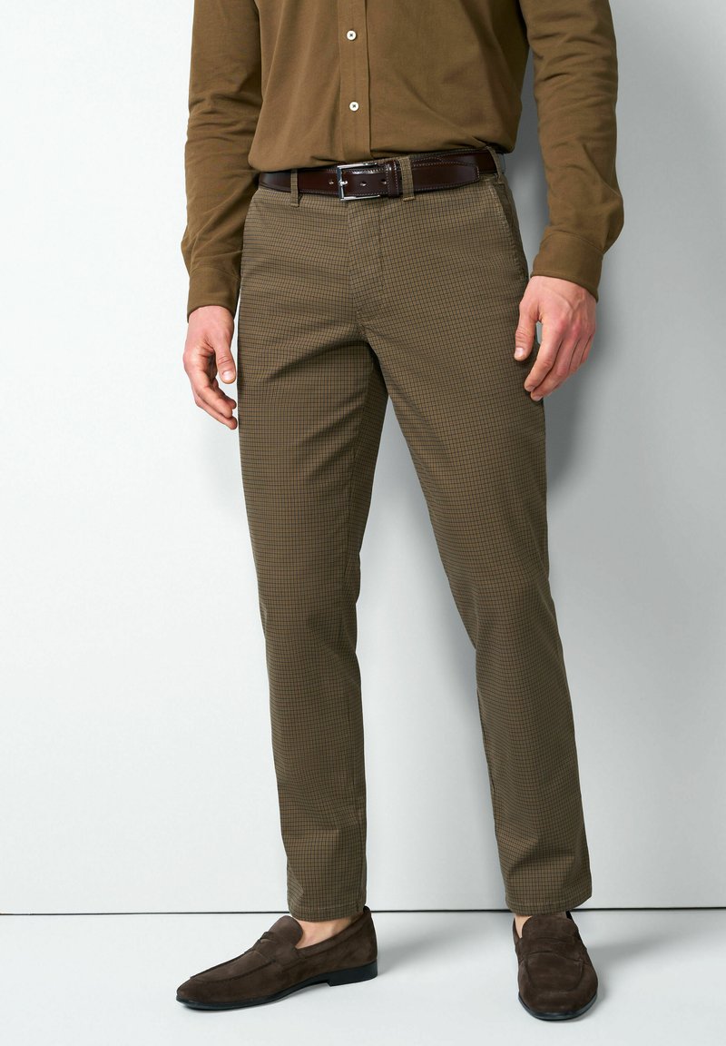 Bruine broek met patroon en een slanke pasvorm, gemaakt van gestructureerde stof, gecombineerd met donkerbruine suède loafers en een bijpassende riem.