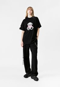 Camiseta negra de gran tamaño con un gráfico de oso texturizado en gris y rosa. Combinada con pantalones negros sueltos y zapatos negros con patrón.