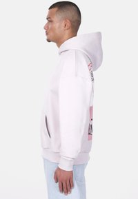 Helle rosa Kapuzen sweatshirt mit Kängurutasche, gerippten Bündchen und hohem Kragen. Mit grafischem Design auf der Rückseite in kontrastierenden Farben.