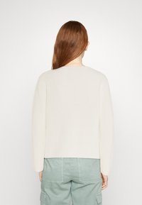 Suéter de canalé en color blanco roto con mangas largas, cuello redondo y dobladillo recto, combinado con pantalones cargo verde claro.