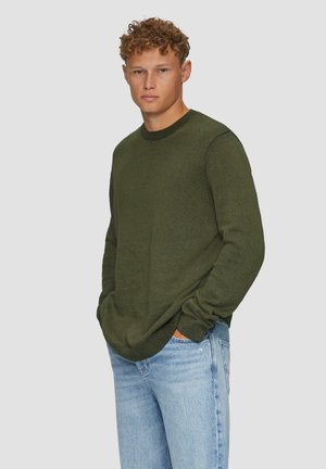 Olive green sweater with a textured knit design, round neckline, and long sleeves, paired with light blue jeans.