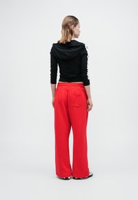 Mustat lyhyet hupparit, joissa on huppu ja valkoiset sivustripit, yhdistettynä löysiin punaisiin sweats-housuihin, joissa on takatasku.
