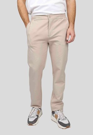 Chinos beige légers avec une texture lisse, taille élastique, poches avant et un design slim, associés à des baskets sportives.