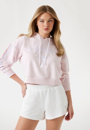 Felpa cropped rosa con logo ricamato, coulisse e maniche a righe, abbinata a pantaloni corti bianchi con vita elastica. Texture liscia, stile casual.