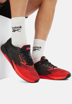 Czarno-czerwone buty sportowe z siateczkową cholewką, sznurowadłami i gumową podeszwą. Do tego białe skarpetki z czarnym logo.