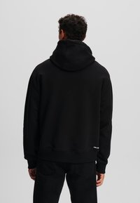 Hoodie noir avec une grande capuche, des poignets et un ourlet côtelés. Fabriqué en tissu doux sans motifs ni logos visibles.