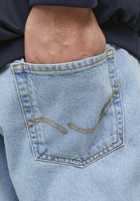 Ljusblå denimficka med kurvig gul sömning, med en fransig textur, mot en mörk tygbakgrund.