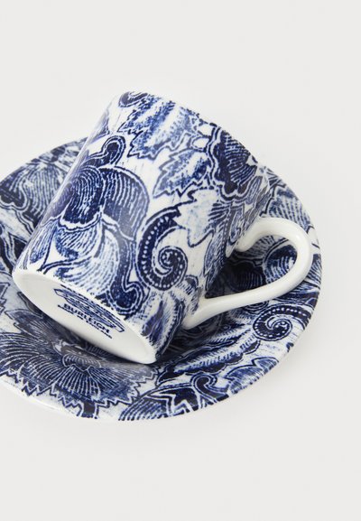 Tazza di porcellana blu e bianca con motivi floreali, su un piattino abbinato; presenta manico curvo e dettagli intricati in tonalità indaco.
