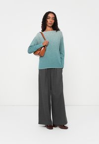 Tealfarbener gradient Strickpullover mit langen Ärmeln, kombiniert mit weit geschnittenen grauen Karohosen. Eine braune rechteckige Handtasche und dunkle Schuhe runden den Look ab.