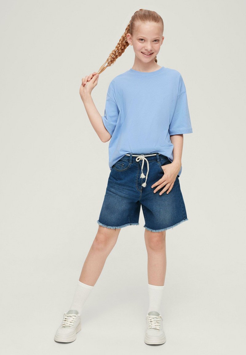 T-shirt bleu clair à manches courtes avec une coupe décontractée, associé à un short en denim bleu foncé de hauteur genou avec des bords effilochés et une taille à cordon.