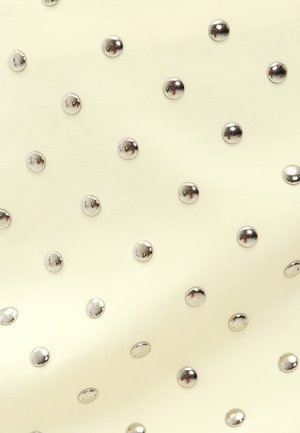 Tissu crème parsemé de clous en argent brillants disposés régulièrement, créant un motif texturé avec une surface lisse dans l'ensemble.