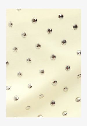 Tissu crème parsemé de clous en argent brillants disposés régulièrement, créant un motif texturé avec une surface lisse dans l'ensemble.