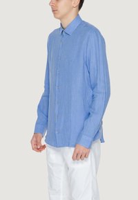 Camicia button-up a righe blu chiaro in tessuto leggero, con colletto a punta e maniche lunghe, abbinata a pantaloni bianchi.