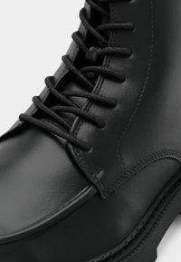 Černá kožená bota s hladkým povrchem, zaoblenou špičkou, pevnými černými tkaničkami a výrazným švem podél podrážky.