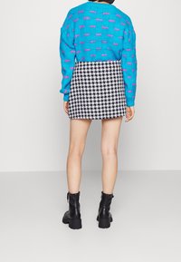 Blauwe gebreide trui met roze accenten, gecombineerd met een zwart-witte hounds-tooth mini rok. Zwarte enkellaarzen maken de outfit af.