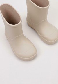Bottes en caoutchouc beige clair avec un bout arrondi, un extérieur lisse et une doublure intérieure douce ; tige courte avec des semelles texturées pour une bonne adhérence.