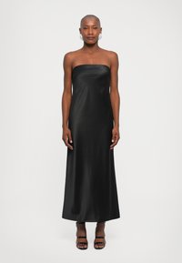 Largo vestido de satén negro sin tirantes con un escote recto y una silueta estilizada. La modelo lleva sandalias negras con tiras.
