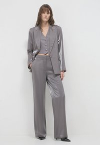 Costume trois pièces gris métallique comprenant un gilet court avec des boutons, un blazer ajusté et un pantalon à jambes larges. Texture lisse et design épuré.