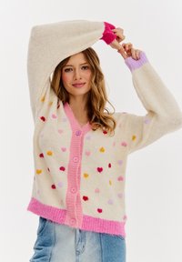 Szydełkowy kardigan w kolorze kremowym z wielokolorowymi wzorami serc, różowy kołnierzyk i listwa guzikowa, ściągacze przy mankietach oraz luźny krój. Miękka faktura.