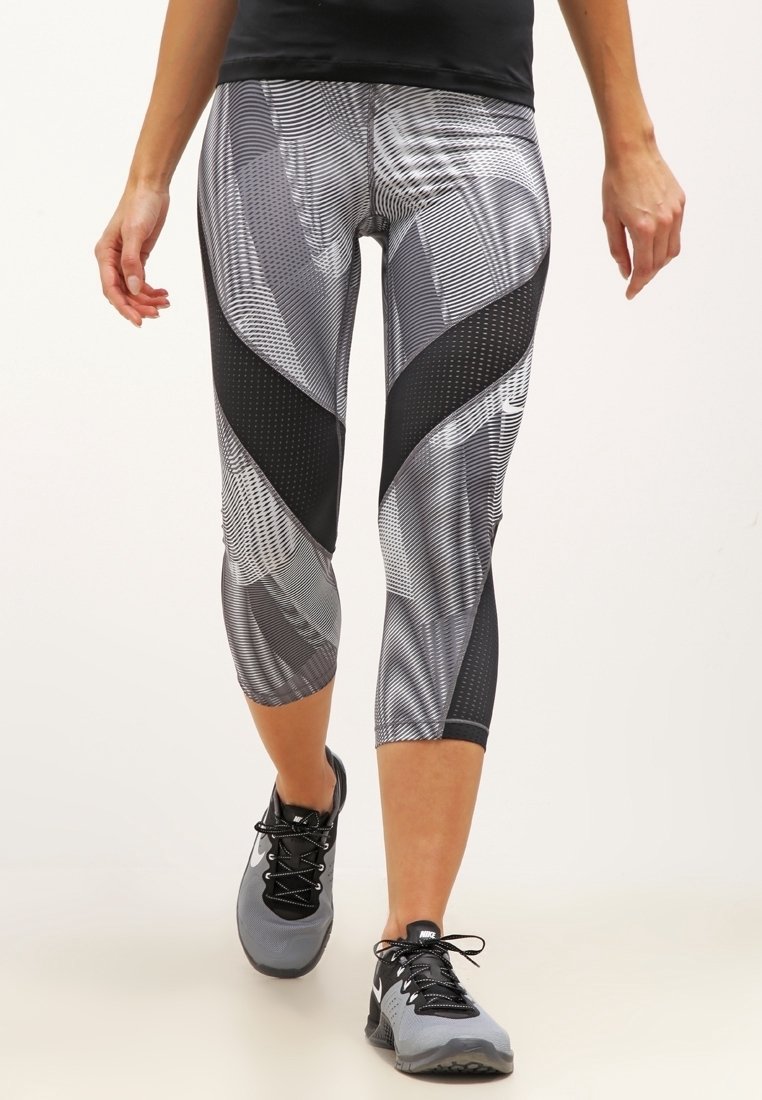 Leggings capri en negro y gris con patrones geométricos y áreas de malla texturizada, combinados con zapatillas deportivas grises.