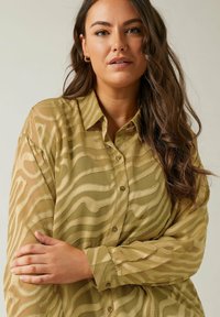 Light olive green blouse with a sheer texture, featuring a wavy pattern, button front, and long sleeves. Soft material with subtle shine.