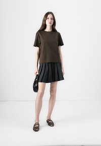Brown short-sleeve t-shirt paired with a black pleated skirt. Model holds a black handbag and wears animal print flat shoes.