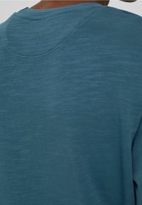 Camisa de manga corta azul con una tela lisa y texturizada, un escote redondo y sutiles variaciones de tono en toda su superficie.