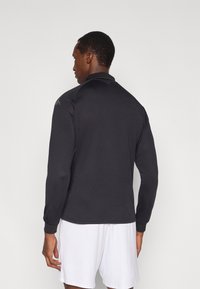 Svart långärmad sporttröja med hög krage, slät textur och figursydd design. Har subtil logodetalj på axeln.