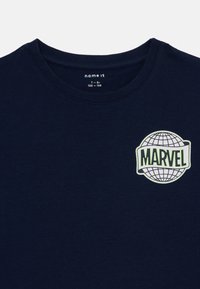 Navy blå bomull T-skjorte med rund hals, med en hvit og grønn "Marvel"-logo med et globusdesign på brystet.