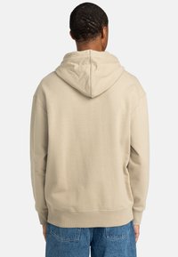 Beige hoodie med snørehætte, blød tekstur, ribstrikkede manchetter og kant, samt løs pasform. Synlige sømme og ingen logoer.