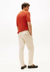 Polo shirt rosso in rete con maniche corte, pantaloni beige e mocassini scuri. Elementi notevoli includono un colletto e dettagli sul retro.