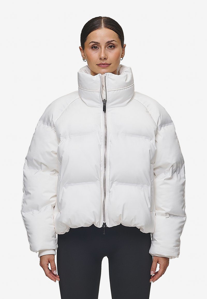 Vit pufferjacka med hög krage, dragkedjestängning och raglanärmar. Den har en quiltad design med synliga sömmar och elastiska ärmslut.