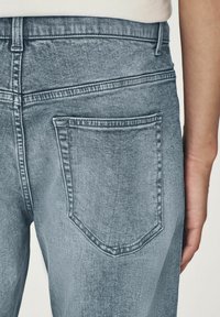 Blugi de denim de un albastru deschis, cu un singur buzunar pe spate cu cusături curbe, talie înaltă și o textură netedă.
