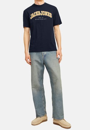 Navy blue cotton t-shirt with "JACK&JONES" printed in yellow, paired with light blue straight-leg jeans and beige slip-on shoes.