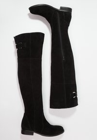 Botas negras de ante por encima de la rodilla. Las características incluyen una cremallera lateral, acentos de metal y un tacón ancho. Textura suave y diseño ajustado.