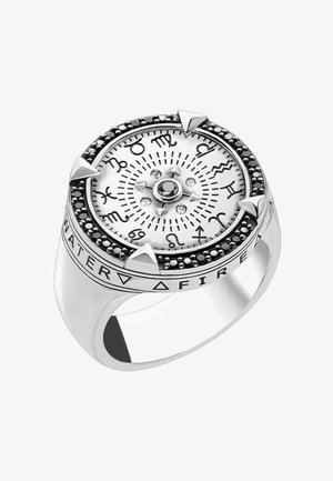 Silberner Ring mit Sternzeichen um ein weißes rundes Zifferblatt, schwarzer Stein in der Mitte, vier dreieckigen Markierungen und Elementsymbolen am Ringband.