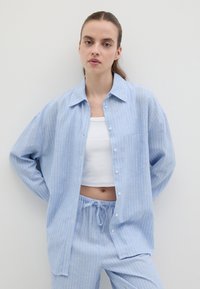 Camicia a righe blu e bianche con bottoni e tasca, abbinata a pantaloni azzurri con coulisse. Tessuto liscio e vestibilità rilassata.