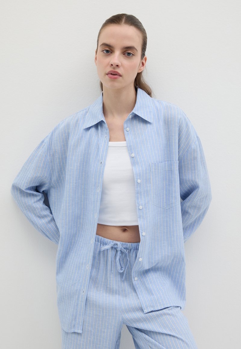 Camicia a righe blu e bianche con bottoni e tasca, abbinata a pantaloni azzurri con coulisse. Tessuto liscio e vestibilità rilassata.