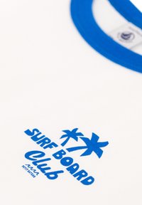 Maglietta bianca con colletto a costine blu. Presenta la scritta blu "SURF BOARD Club" e grafica di palme. Texture in cotone morbido.