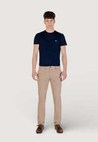 Camiseta de cuello redondo en color navy combinada con chinos beige claros y zapatos de barco marrón. Incluye un diseño ajustado y un pequeño logo en la camiseta.