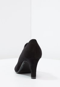 Chaussure à talon haut en suede noir avec un bout pointu, un design incurvé et une partie supérieure texturée. Le talon mesure environ 8 cm.