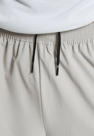Shorts gris clair avec une ceinture élastique et des cordons noirs, présentant une texture lisse et douce ainsi qu'un design subtil avec un tissu légèrement froncé.