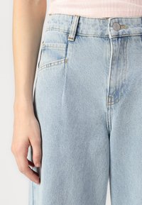 Vaaleansiniset farkut rentoa istuvuutta, joissa on etutasku, kuparinväriset ompeleet ja metallinen nappisuljenta vyötäröllä.