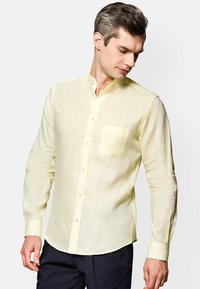 Jasnożółta koszula z długim rękawem, wykonana z lnu, z kołnierzykiem mandarynkowym, kieszenią z przodu i zapięciem na guziki. Gładka tekstura i luźny fason.