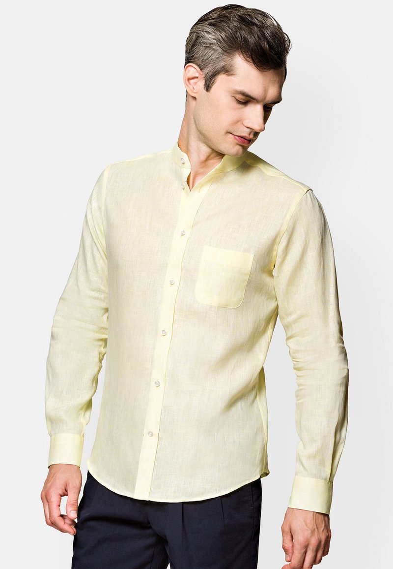 Jasnożółta koszula z długim rękawem, wykonana z lnu, z kołnierzykiem mandarynkowym, kieszenią z przodu i zapięciem na guziki. Gładka tekstura i luźny fason.