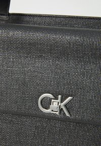 Black textured handbag with a silver hardware detail featuring the initials "CK." The material has a woven look and structured design.