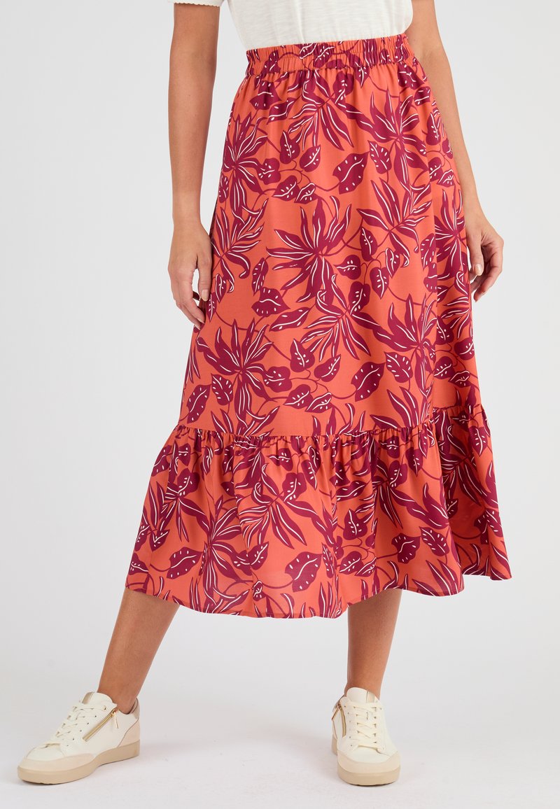 Oranje maxi rok met een bloemenpatroon in donkerpaars, met een gerafelde zoom en een elastische tailleband. Gecombineerd met witte sneakers.