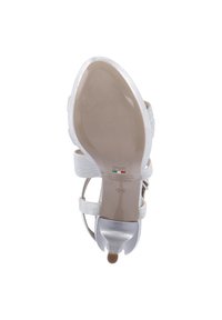 Scarpa con tacco alto argento con cinturini alla caviglia, superficie metallica liscia, punta affilata e una suola leggera beige con dettagli di branding.