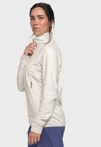 Helle beige Zip-Jacke mit hohem Kragen, schlanker Passform und strukturiertem Stoff. Verfügt über eine Seitentasche mit Reißverschluss und lange Ärmel.