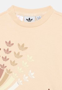 Sweatshirt beige clair avec un col rond et un dégradé de motifs de logo dans des nuances de marron et de crème sur le devant.